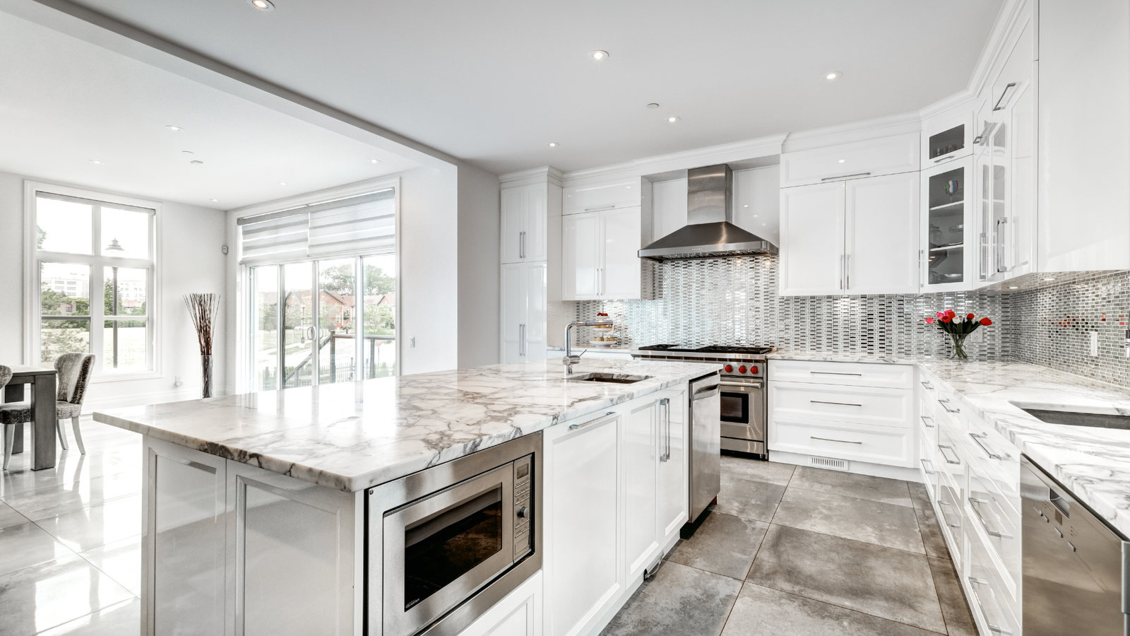Modern kitchen in California with white cabinets, marble countertops, stainless steel appliances, a dining area, and large windows.