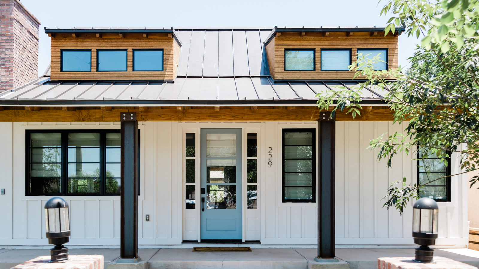 Modern white house in California with a light blue door, black-framed windows, metal roof, and wooden accents at the entrance.