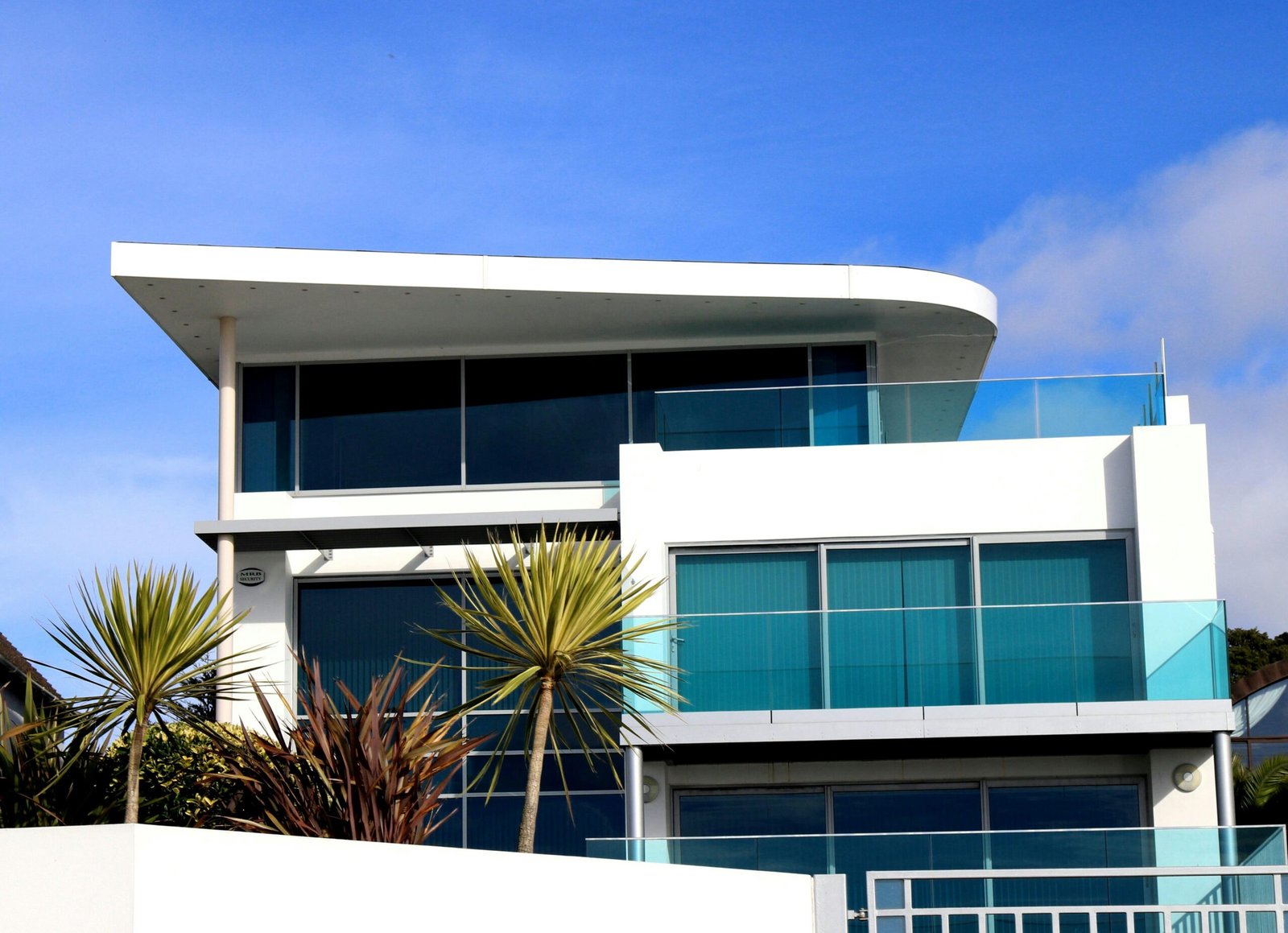 Modern two-story white house in California with blue-tinted windows, palm trees, and a clear blue sky.