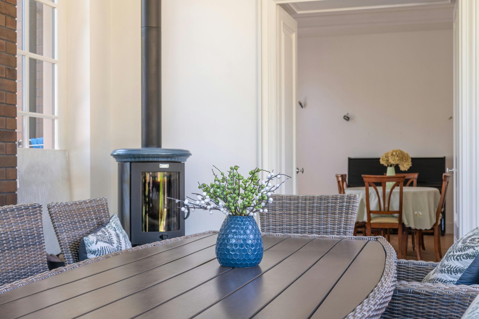 Southern California indoor patio with a wicker dining set, blue vase, small fireplace, and a dining room in the background.