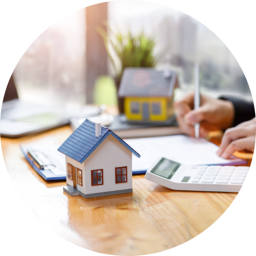 a miniature of a house and a person writing down to a paper with calculator.