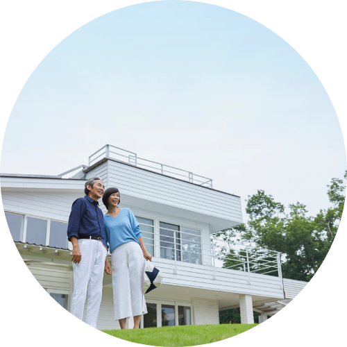 A happy couple stands on a grassy lawn in front of a modern two-story white house. The sky is clear, and the mood is joyful and serene.