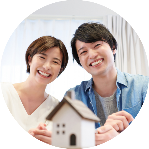 A smiling couple sits together indoors, holding a small model house.